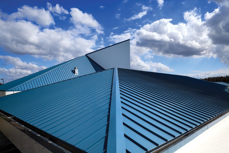 A blue corrugated metal rooftop with angular designs under a bright blue sky filled with white clouds.