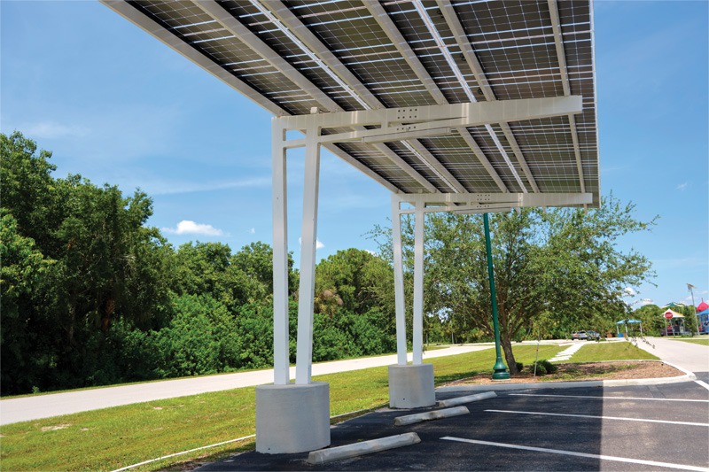 A canopy over a parking area with green trees and a clear blue sky in the background.