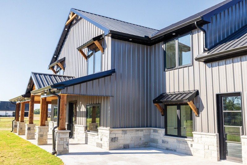 Modern two-story house with a metal and stone exterior, featuring large windows, a sloped roof, and a front porch with wooden columns.