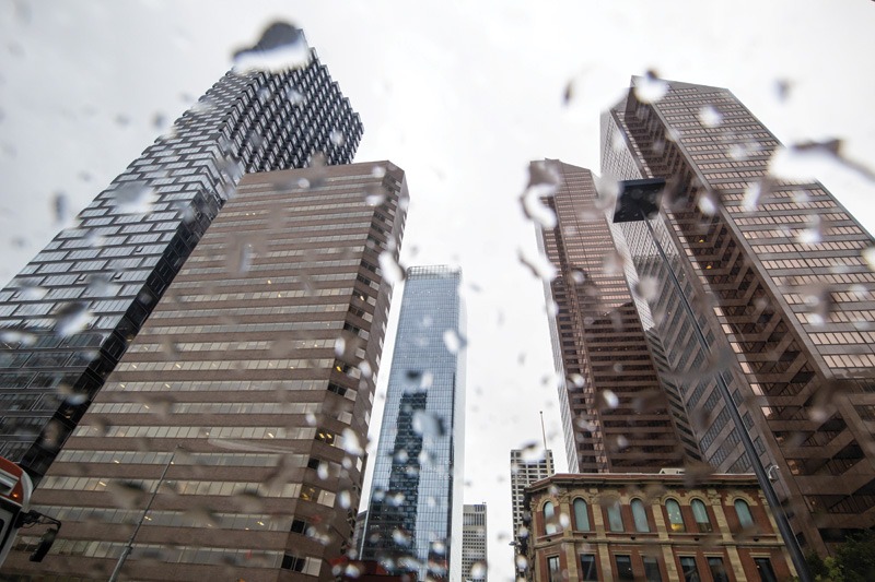 Tall skyscrapers viewed from the ground, seen through raindrops on glass, under an overcast sky.