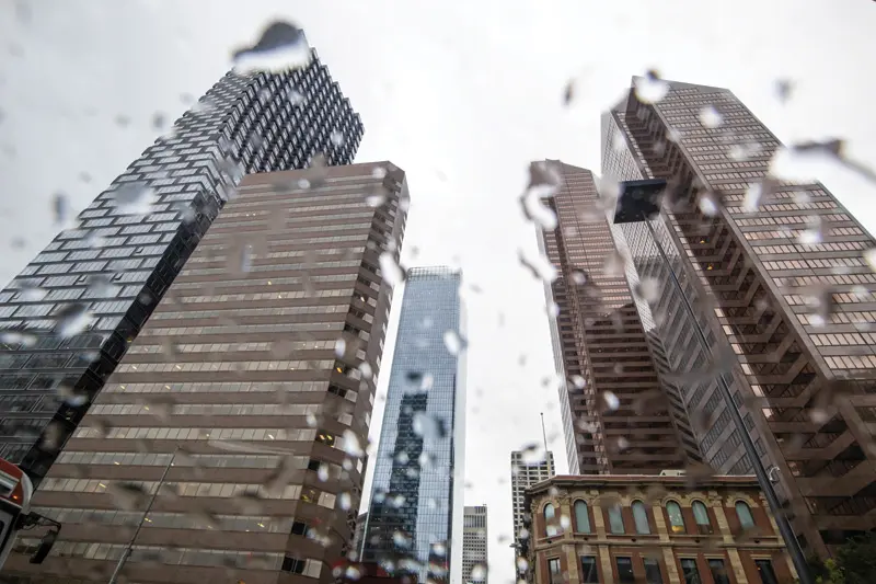 Tall skyscrapers viewed from the ground, seen through raindrops on glass, under an overcast sky.