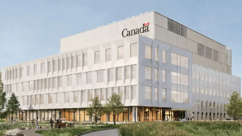 A modern white building with geometric windows, featuring the word "Canada" and the Canadian flag at the top, surrounded by greenery and people sitting on benches.