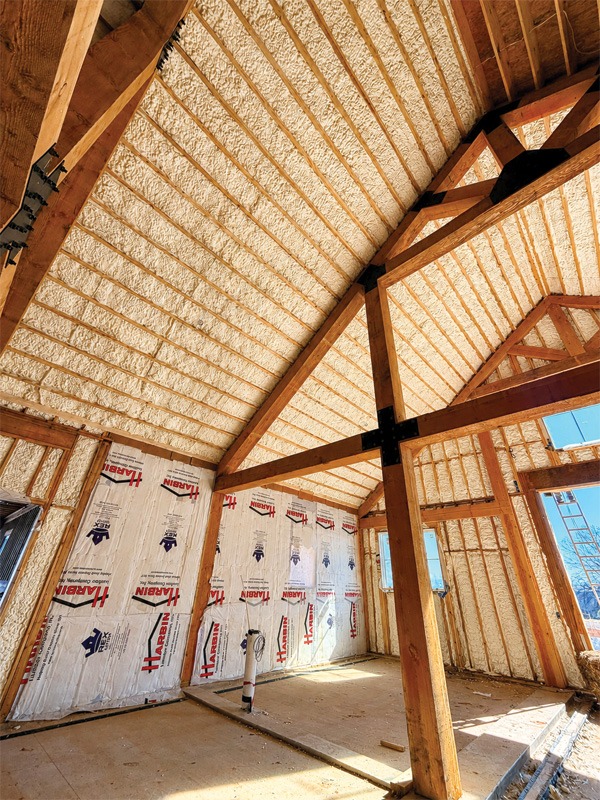 Interior view of a partially constructed building with a textured white ceiling, exposed wooden beams, and foil insulation on the walls, illuminated by natural light.