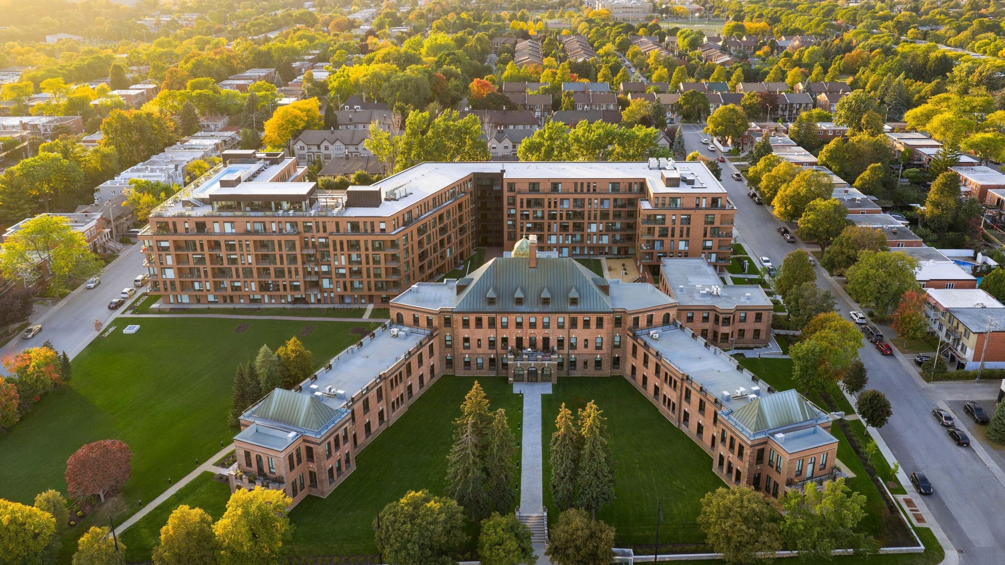 Aerial view of a brick campus building and landscaped courtyard surrounded by autumn-colored trees and residential streets.