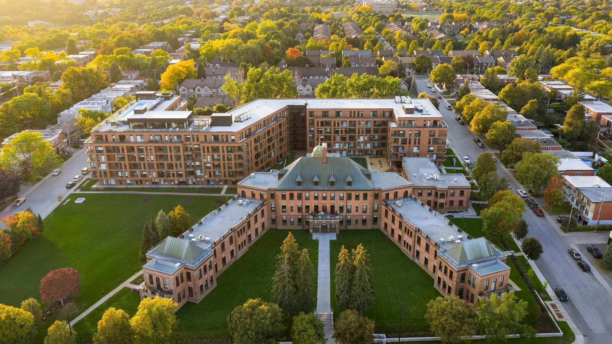 Aerial view of a brick campus building and landscaped courtyard surrounded by autumn-colored trees and residential streets.