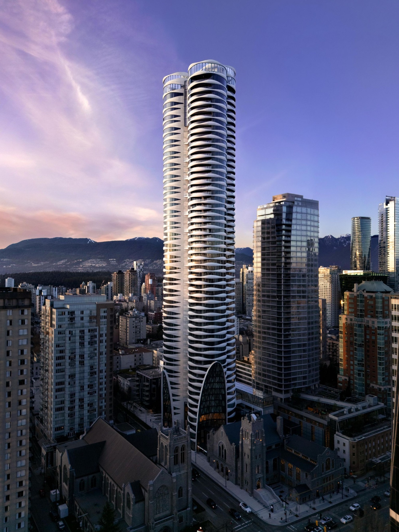 City skyline at dusk featuring a distinctive white tower with curved balconies, surrounded by high-rises, a stone church, and snow-dusted mountains.