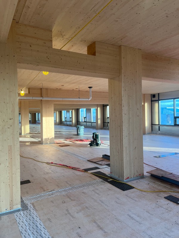 Unfinished open interior with exposed timber framing, large windows, construction equipment, cables, and materials on the floor.