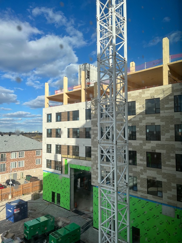 Construction site with a tall steel tower crane in front of a partially completed multi-story building.