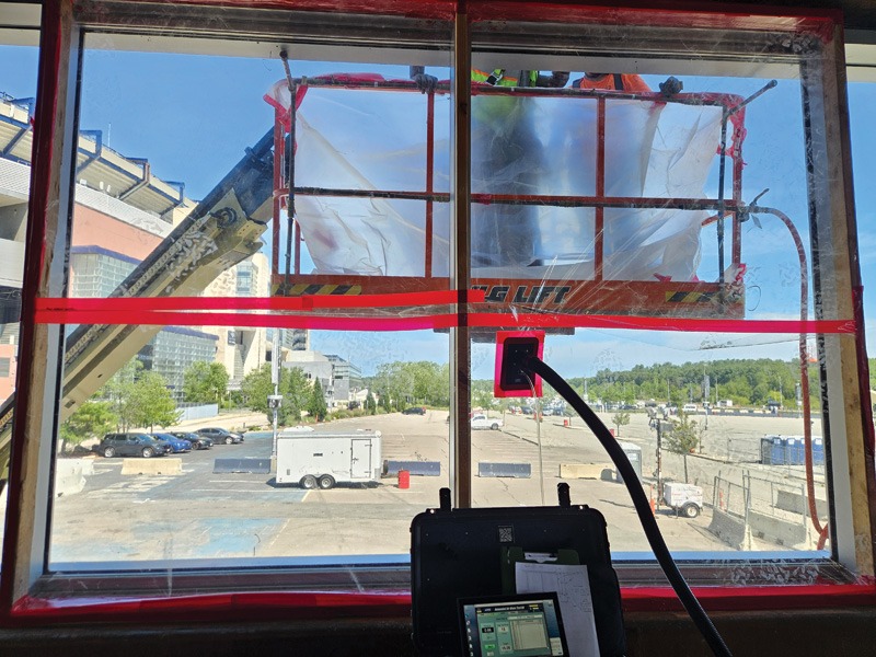 View from inside a construction lift, showing a red aerial platform, control console, and construction area through the window.
