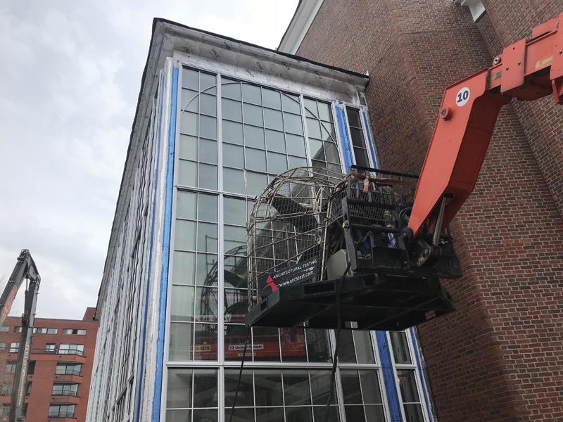 A construction lift platform is raised beside a large industrial building with a tall, multi-pane glass window wall.