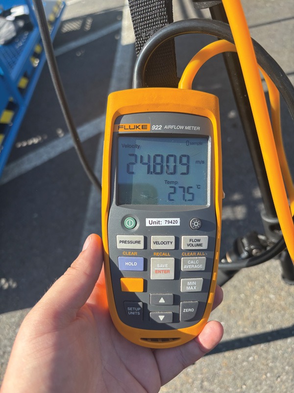 Handheld Fluke 922 airflow meter displaying 248.09 m/s velocity and 27.5°C temperature, with orange and black cables attached.