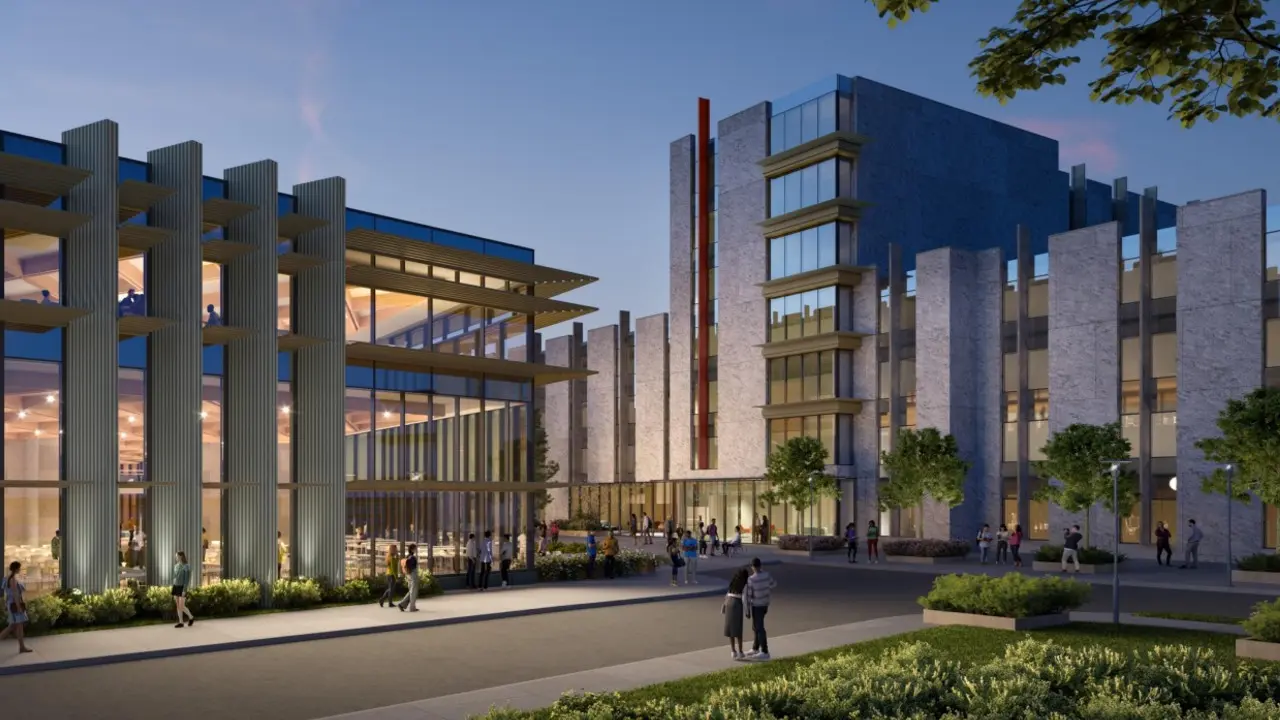 Modern illuminated campus complex with glass façades, gray stone buildings, landscaped plaza, and pedestrians at dusk.