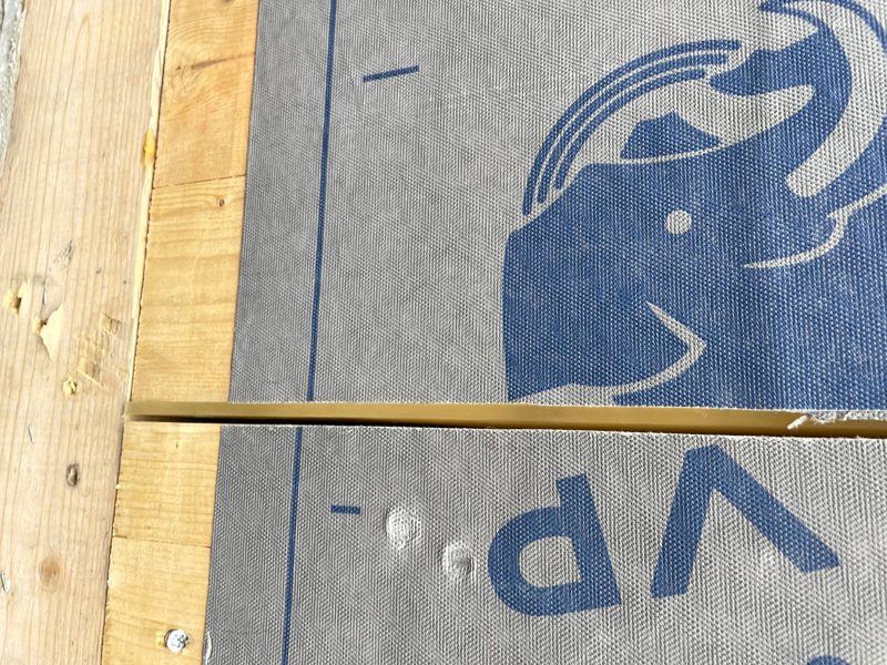 Close-up of gray mesh panels with a blue graphic and partial lettering, divided by a vertical wooden strip above unfinished wooden boards.