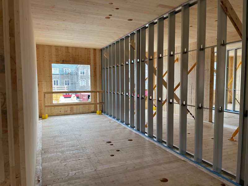 Unfinished wood-framed room with plywood walls, exposed metal ceiling joists, and a window opening at the far end.
