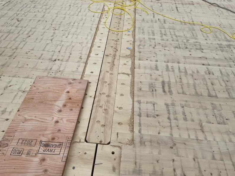 Construction floor with exposed wood framing, a plywood sheet, and a yellow electrical cord.